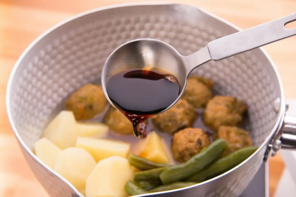 A ladle pouring dark soy sauce onto vegetables.