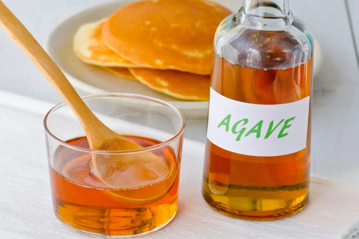 A bottle of agave nectar with a glass serving cup.