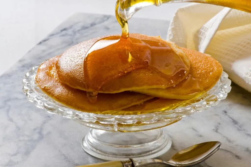 A glass serving plate of pancakes served with agave syrup.