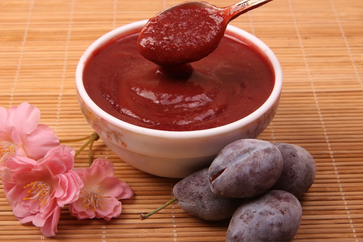 A bowl of Chinese plum sauce with a side of plums.