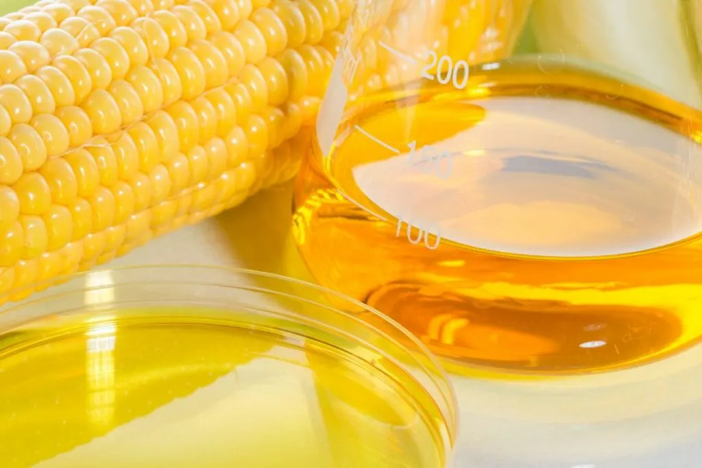 A borosilicate glass of corn syrup with a corn cob on the side.