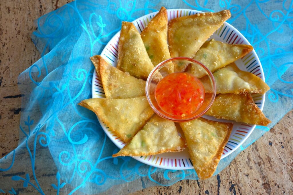 A plate of fried wontons with sweet chili sauce.