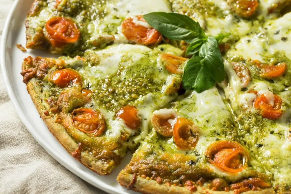 A green pesto pizza -with mozzarella and tomatoes.