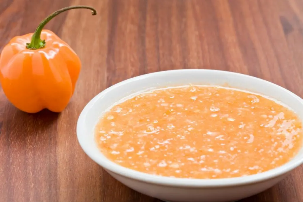 A bowl of habanero sauce with a scotch bell pepper.