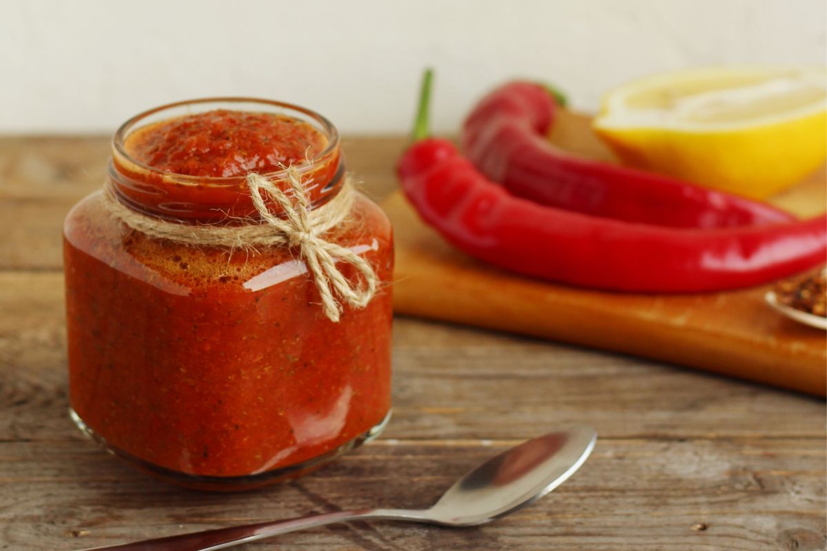 A jar of harissa sauce with peppers on the side.