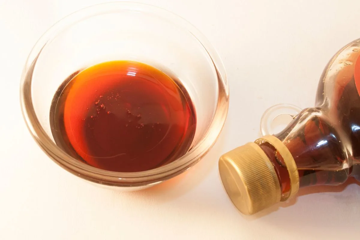 A bowl of maple syrup with a bottle of it next to it.