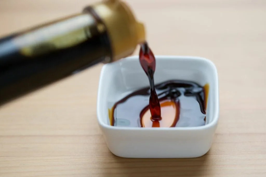 A bottle of soy sauce being poured into a sauce bowl.