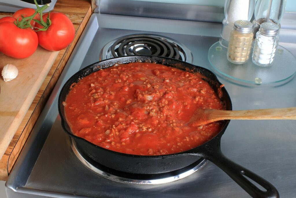 A pan of spaghetti sauce simmering on a stove top.