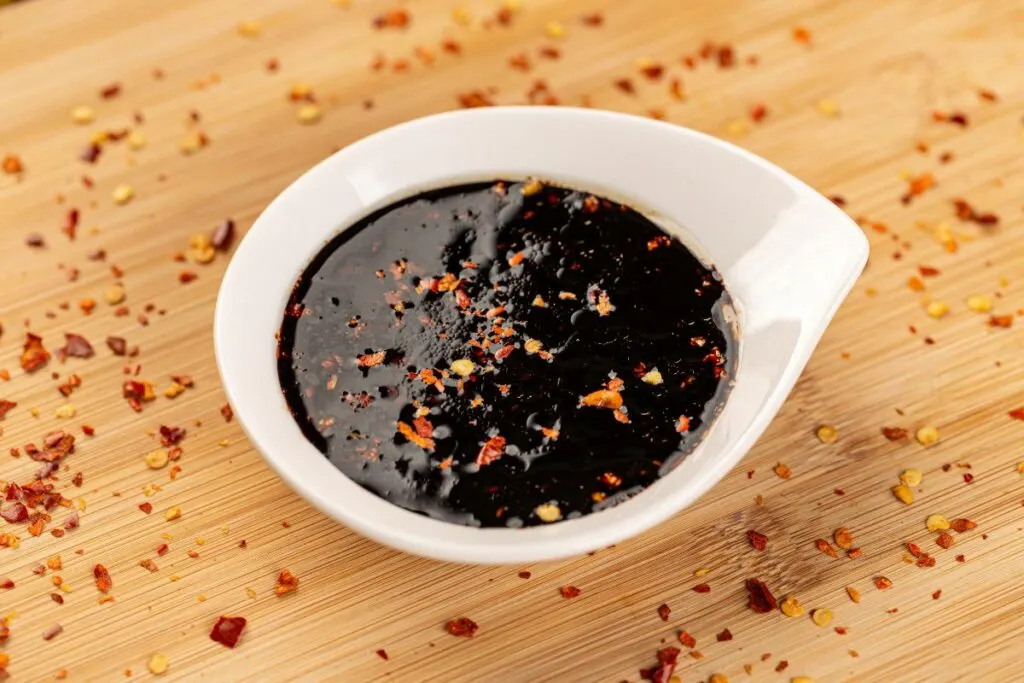 A sauce bowl of teriyaki sauce with pepper shavings.