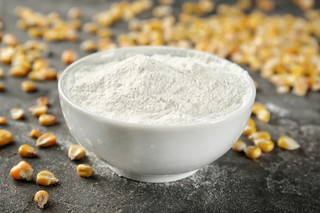 A bowl of cornstarch with corn kernels scattered around.