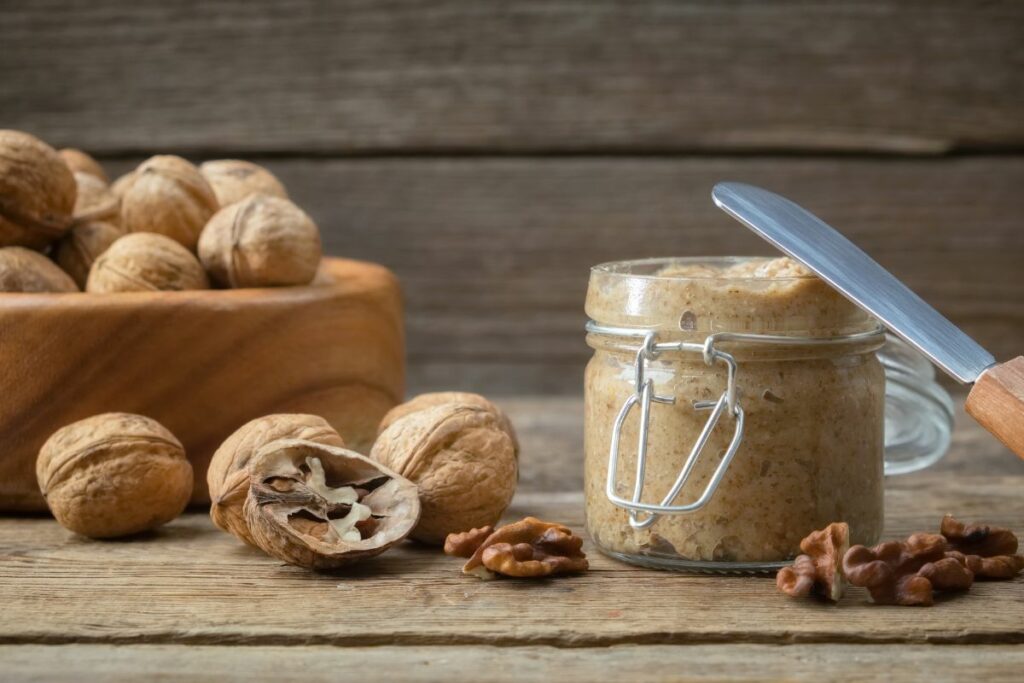 A glass jar of walnut butter with open walnuts next to it.