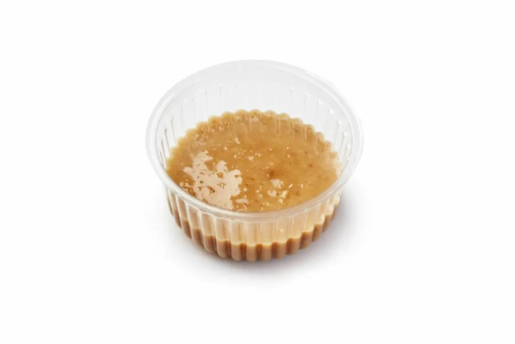 A plastic cup of peanut dipping sauce.