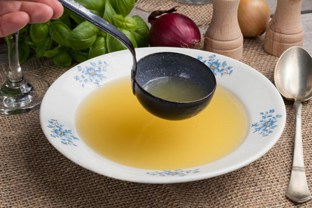 A saucer of tasty chicken broth with a ladle.