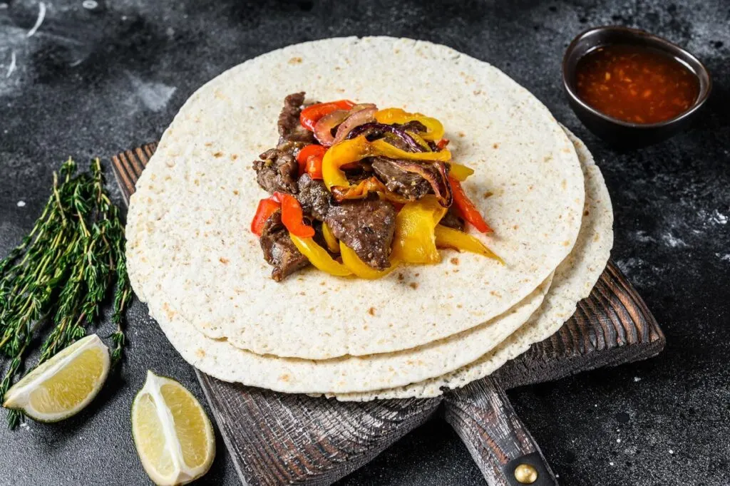 A wooden pizza board with beef steak fajitas on top.