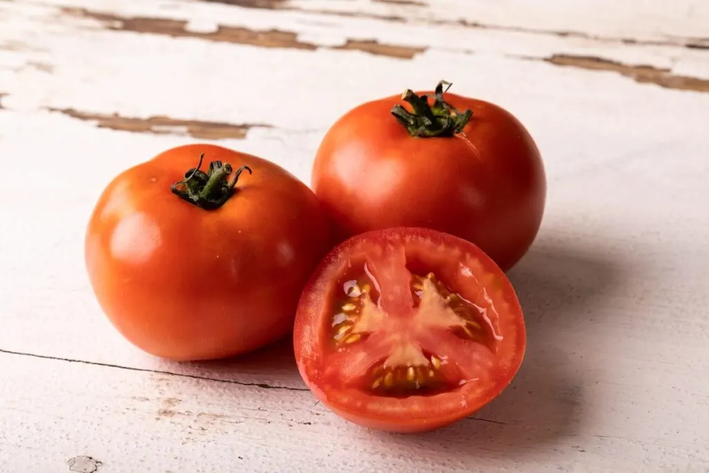 A closeup of 3 fresh red tomatoes on a wooden table.