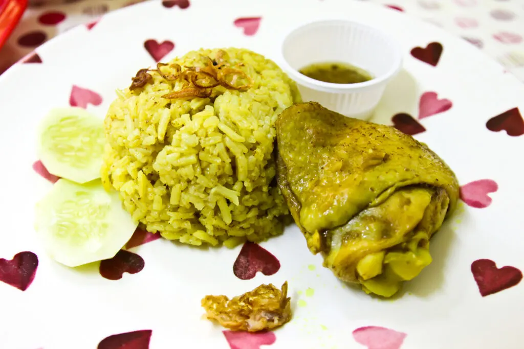 A plate of homemade Thai chicken biryani with chopped cucumber and sauce.