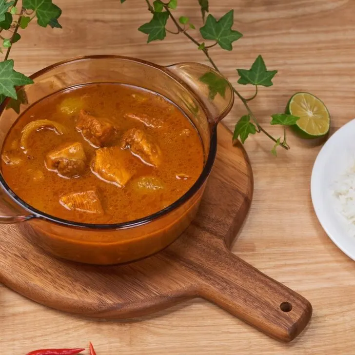 A glass pot of tasty chicken curry with a plate of rice next to it.