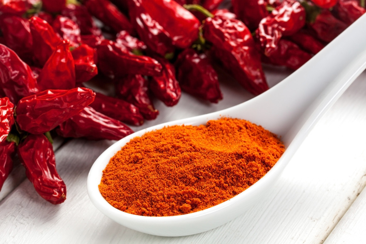 A spoon of paprika powder with some dried peppers in the back.