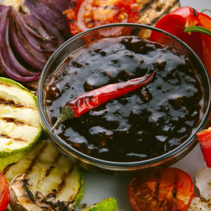 A glass sauce bowl of teriyaki sauce with various roasted ingredients.