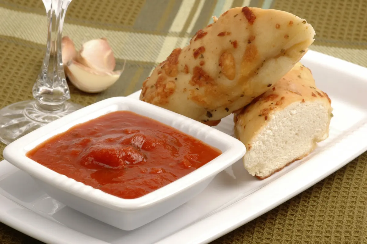 Marinara sauce in a bowl next to garlic bread.