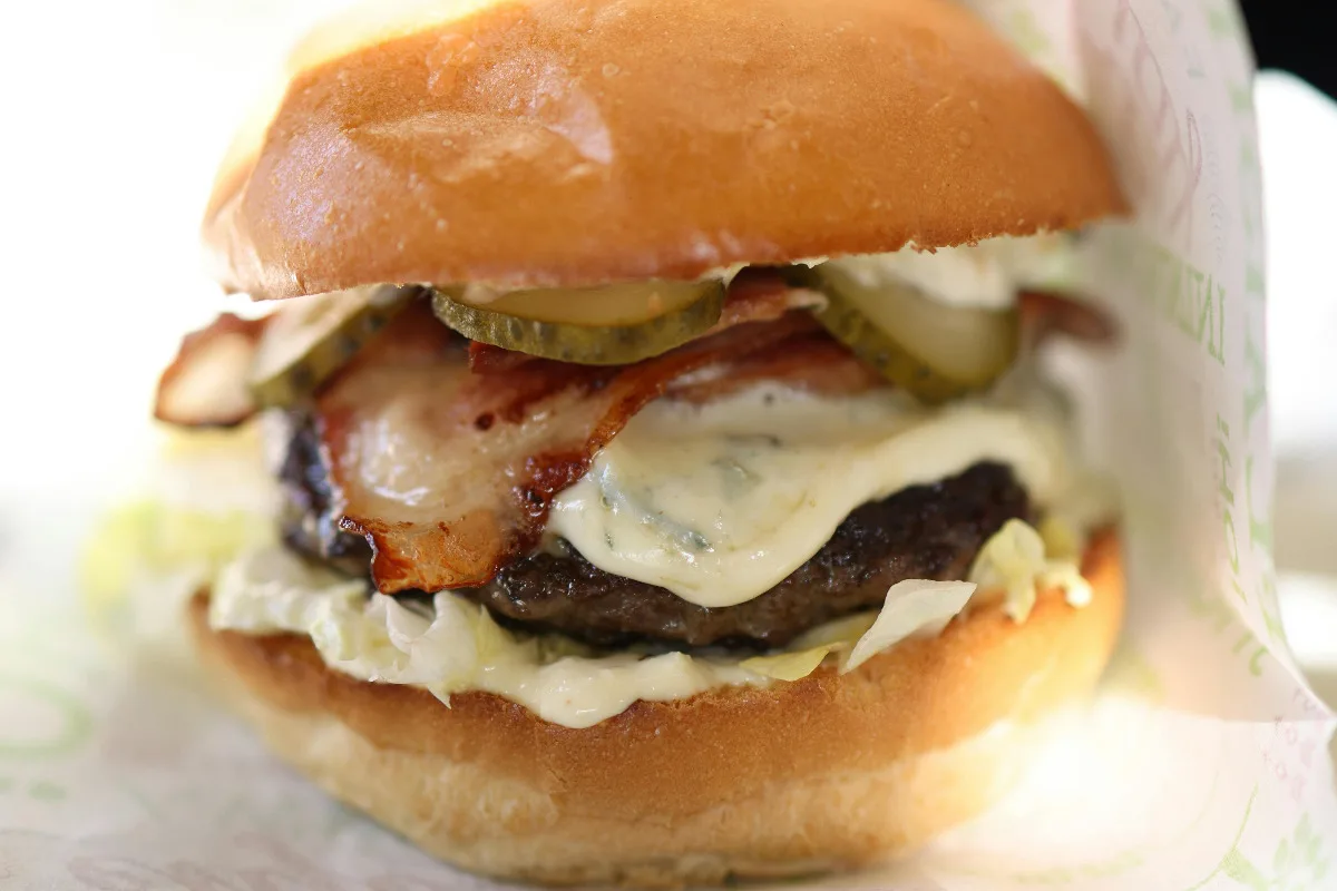 A closeup of a delicious sonic bacon burger with ranch dressing inside.