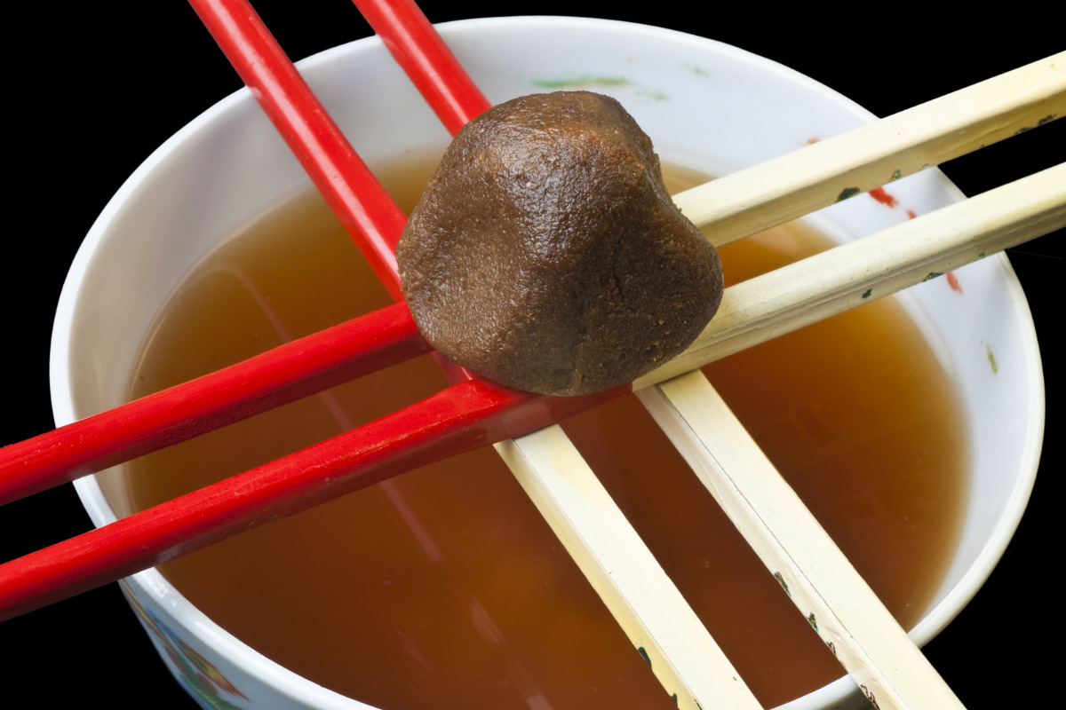 A delicious bowl of miso soup with chopsticks laid across it and a ball of miso paste in the middle.