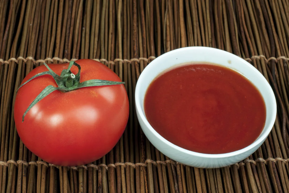 A bowl of rich tomato sauce with a fresh tomato next to it.