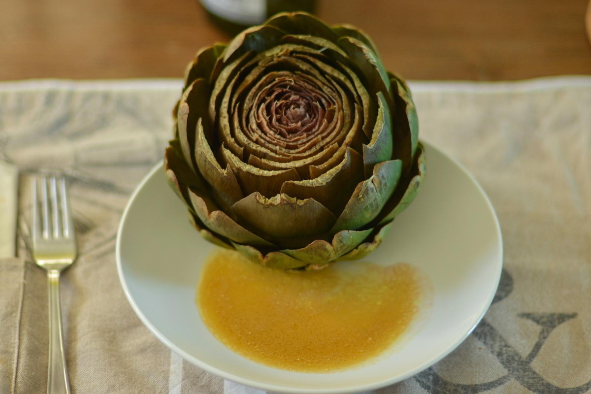 A whole artichoke on a plate with a drizzle of vinaigrette.