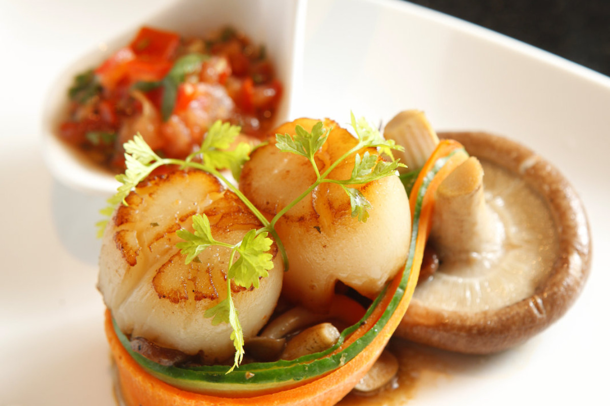 A plate of scallops with mushroom and a serving spoon of tomato basil sauce.