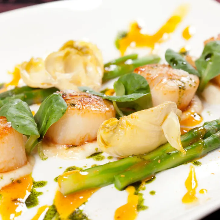 Delicious pan-fried scallops garnished with asparagus and sauce.