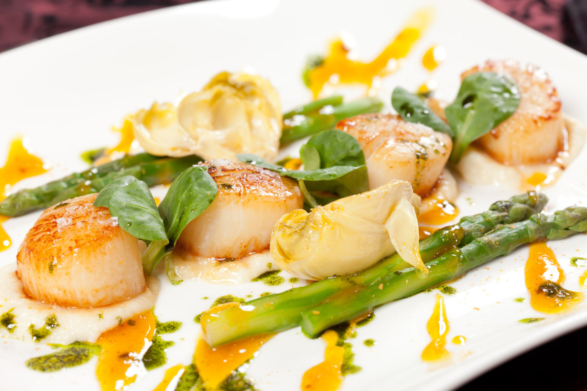 Delicious pan-fried scallops garnished with asparagus and sauce.
