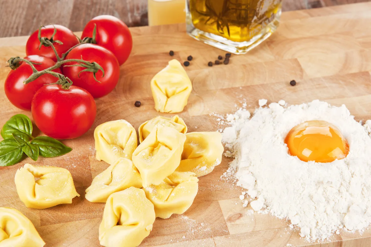A wooden tray of tortellini and ingredients for making a dish.