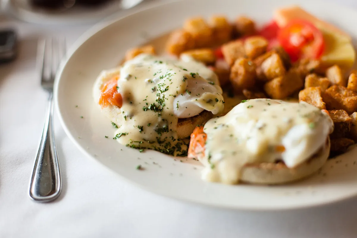 A plate of egg benedict with grilled salmon and a creamy lemon butter sauce.