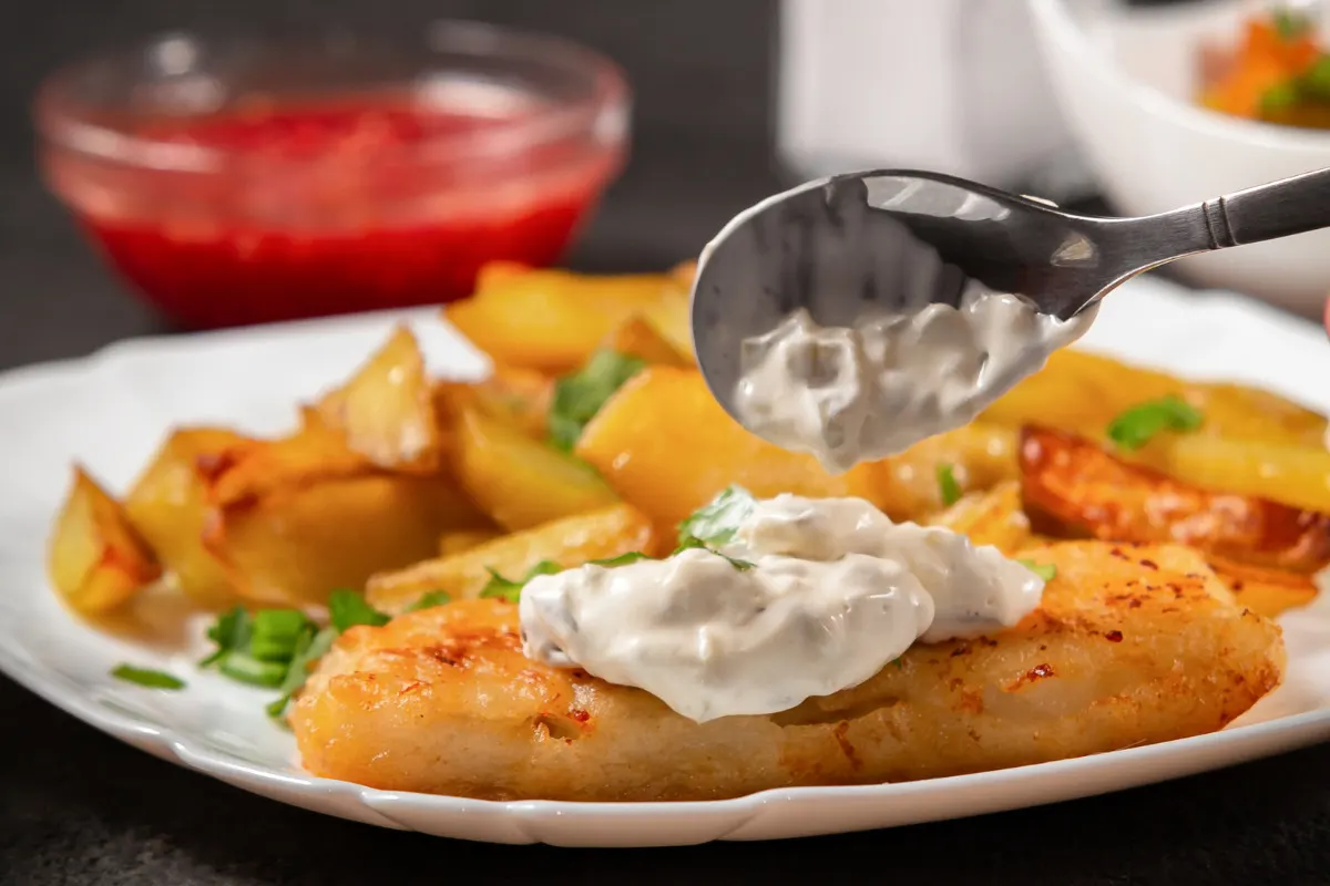 A plate of fish and chips topped with a spoonful of creamy tartar sauce.