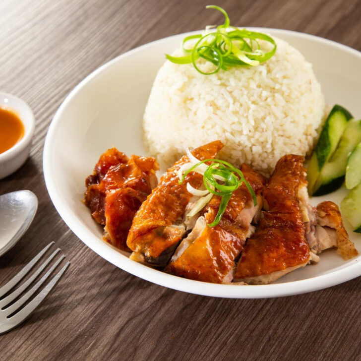 Chicken on a plate of rice and cucumber with peanut sauce.