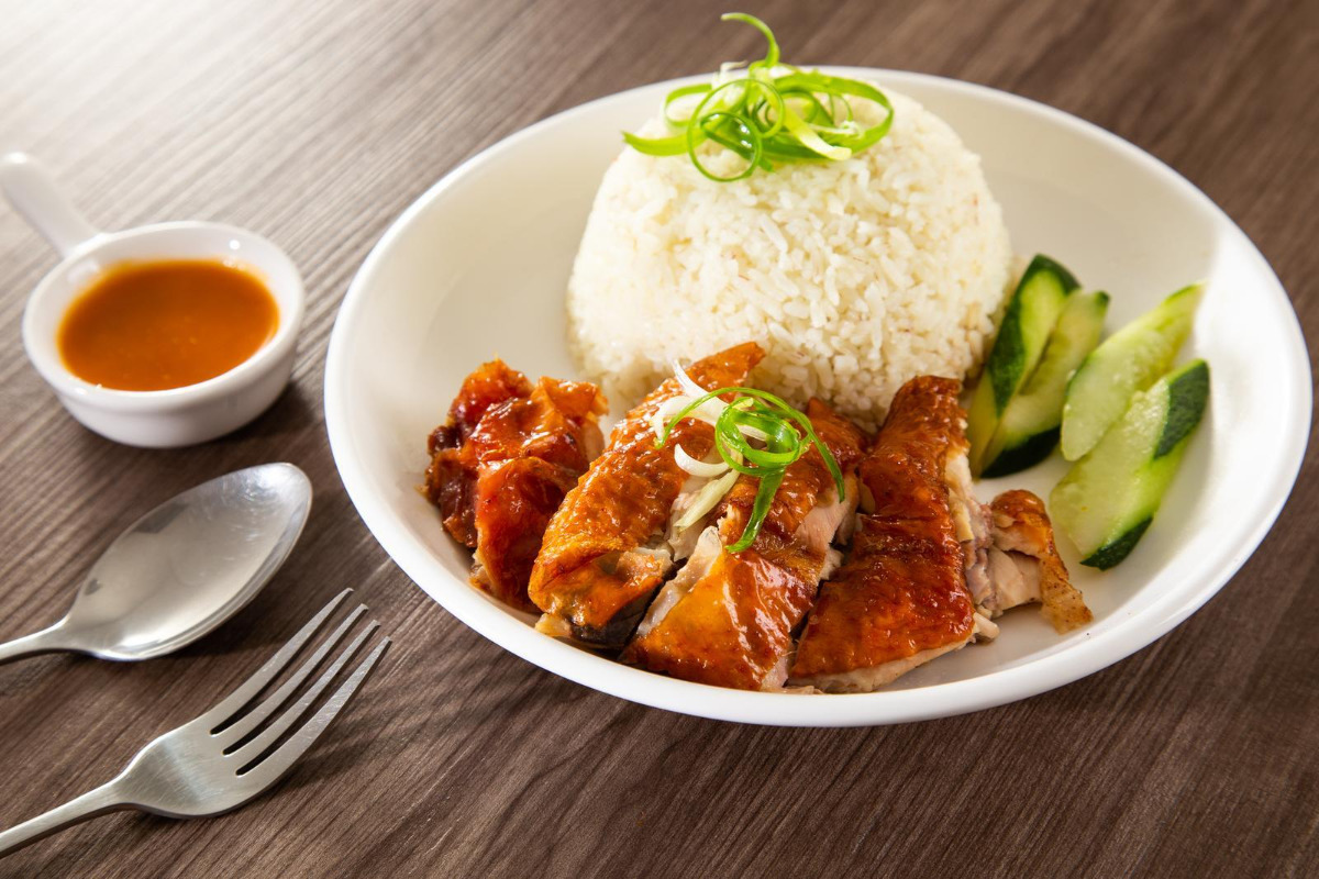 Chicken on a plate of rice and cucumber with peanut sauce.