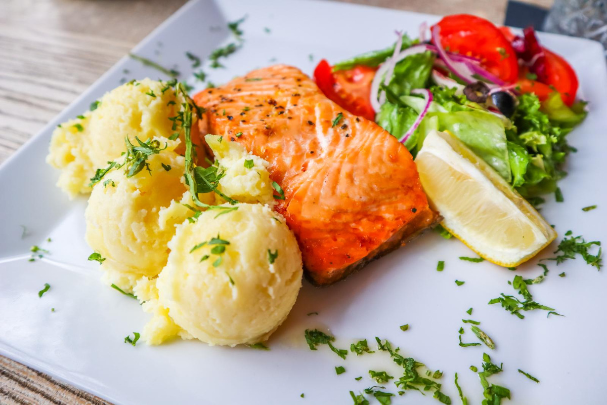 A delicious plate of baked salmon with mashed potatoes, tomatoes, red onions, olives and salad leaves.