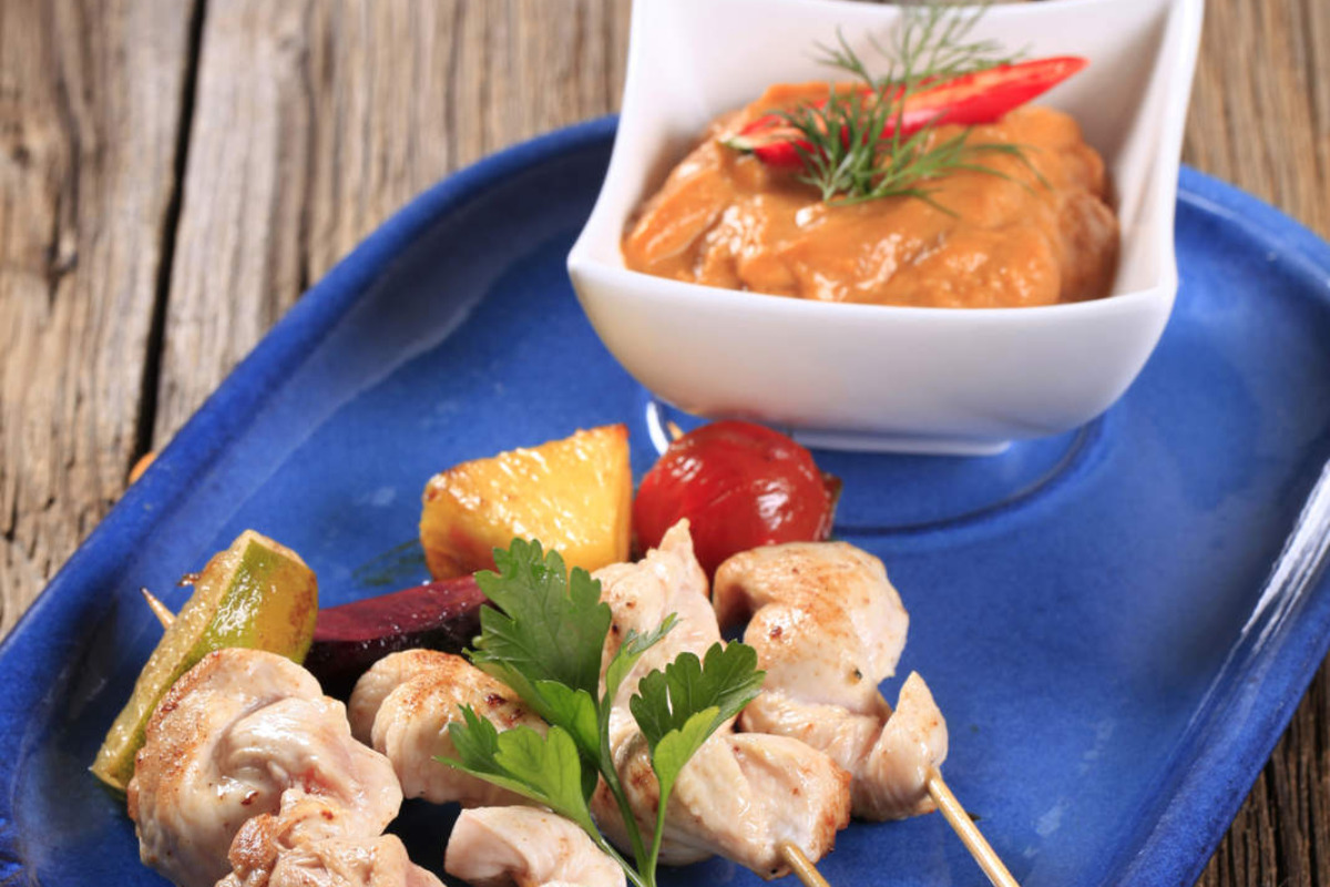 A plate of chicken skewers with a sauce bowl of Romesco sauce.