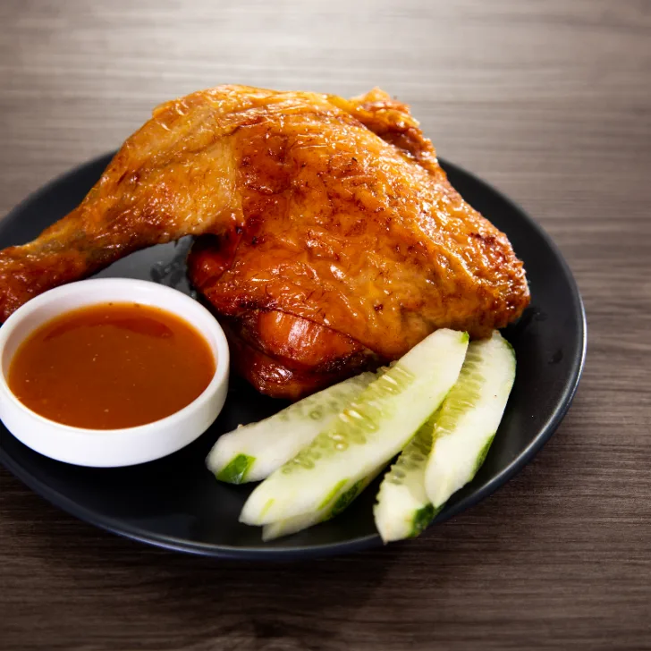 A whole chicken leg on a plate with cucumber and sweet and sour sauce.