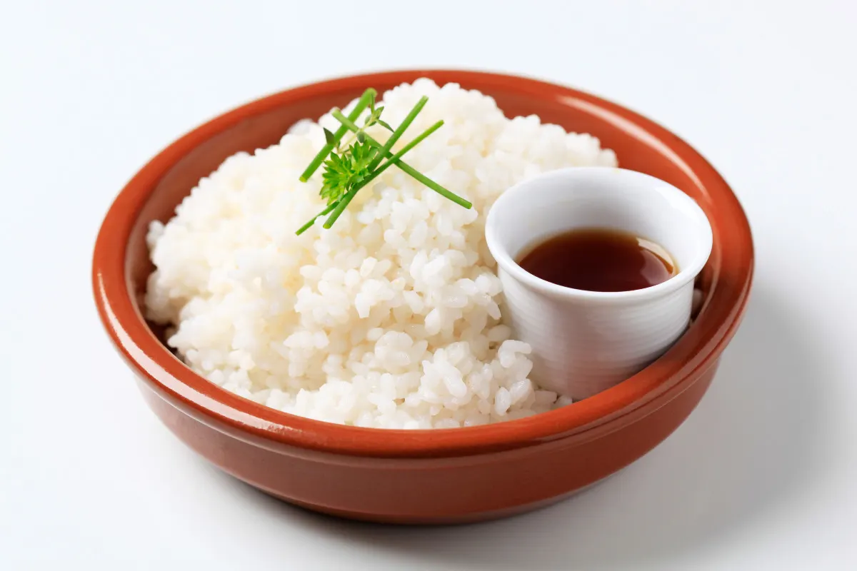 A bowl of rice and a sauce bowl of soy sauce.