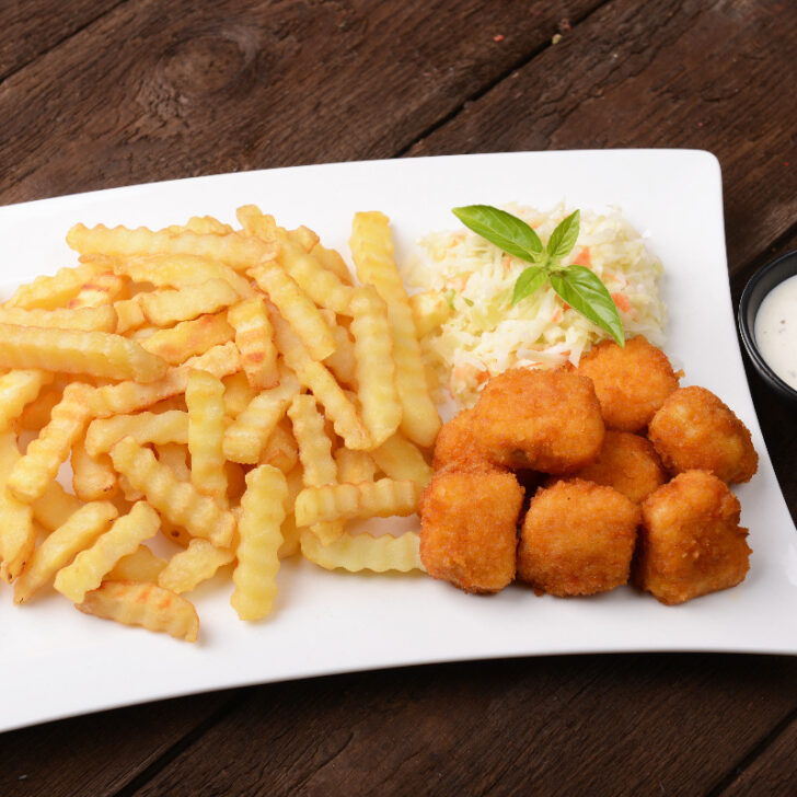 A plate of crispy nuggets, fries, and coleslaw with a side of ranch dressing.