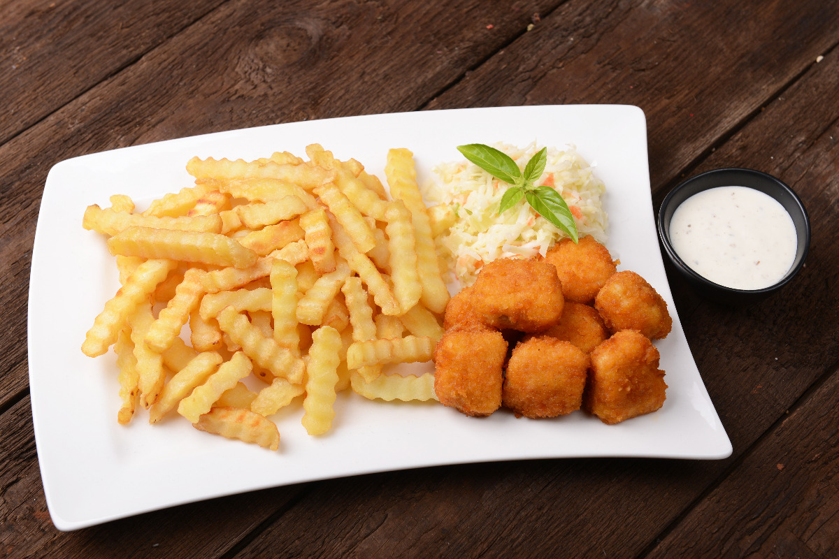 A plate of crispy nuggets,  fries, and coleslaw with a side of ranch dressing.