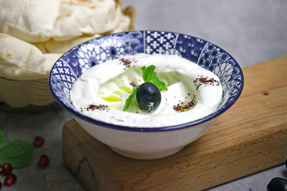 Creamy bowl of yogurt dressing topping with herbs and an olive.