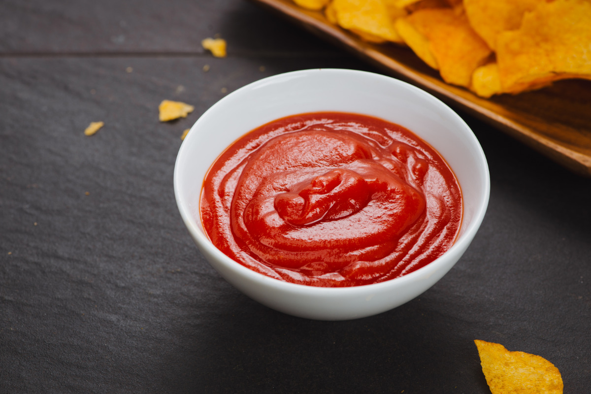 A sauce bowl of ketchup with a sided of chips.