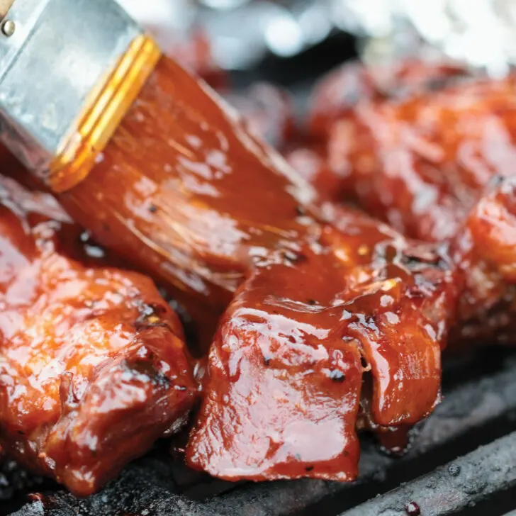 Ribs on a grill being brushed with BBQ sauce.