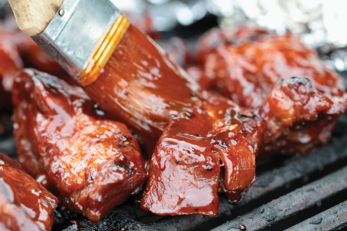 Ribs on a grill being brushed with BBQ sauce. 